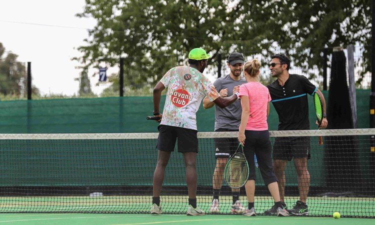 Four people shaking hands on a tennis court at the net