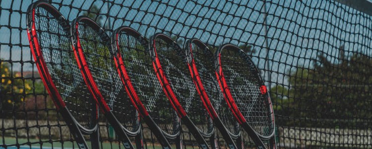 close up of 6 dunlop black and red tennis rackets placed  leaning on tennis net