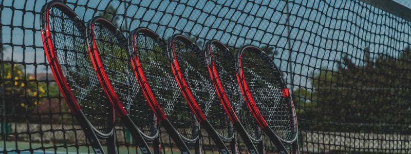 close up of 6 dunlop black and red tennis rackets placed  leaning on tennis net