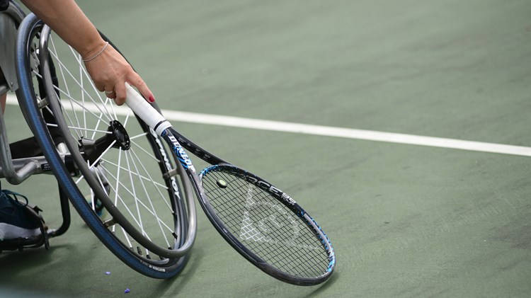 Close-up image of wheelchair on court with a tennis racket