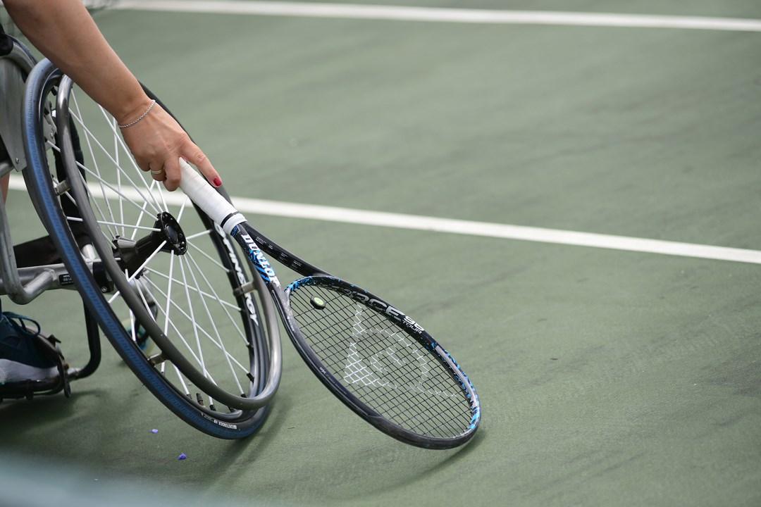 Close-up image of wheelchair on court with a tennis racket
