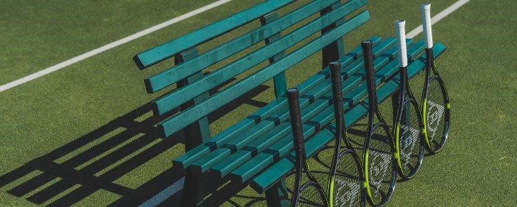 yellow and black dunlop tennis rackets lined up against a green bench on tennis court