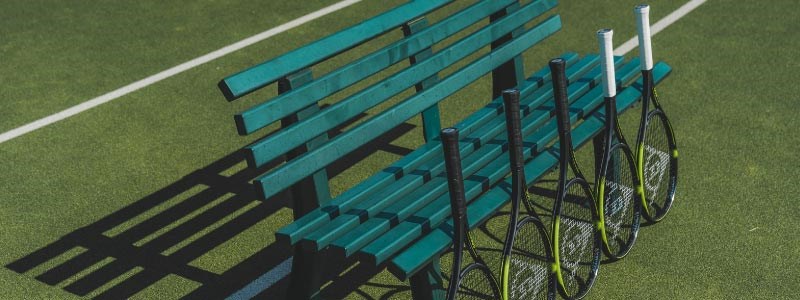 yellow and black dunlop tennis rackets lined up against a green bench on tennis court