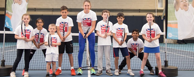 Johanna Konta with a group of children, all holding tennis rackets in front of a tennis net on a court
