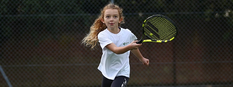 Young girl playing tennis with a black and yellow racket