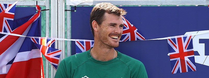 jamie murray smiling looking to the side with mini GB flags hanging  and LTA logo behind him 