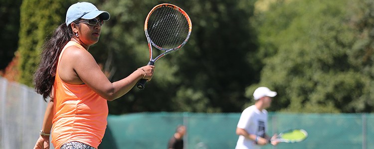 Woman in an orange vest playing tennis on a sunny day