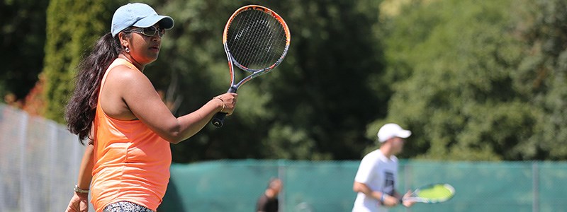 Woman in an orange vest playing tennis on a sunny day