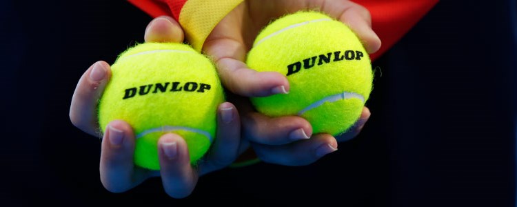 close up image of two dunlop tennis balls held in hands that are crossed