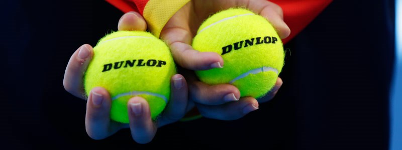 close up image of two dunlop tennis balls held in hands that are crossed