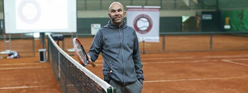 Leonardo Azevedo smiling on a tennis court holding a tennis racket