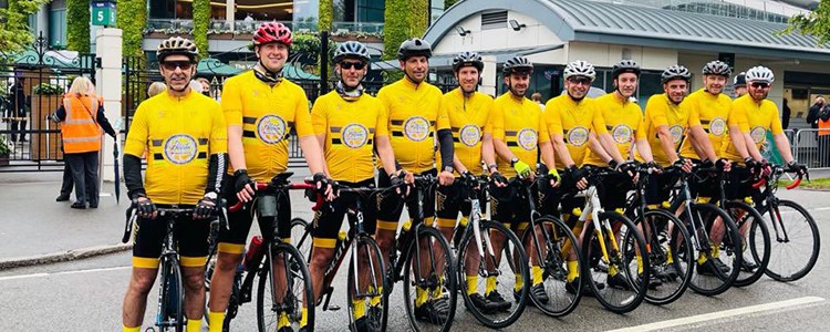 rutherglen peloton team standing on their bikes lined up outside wimbledon with yellow shirts and bike helmets on