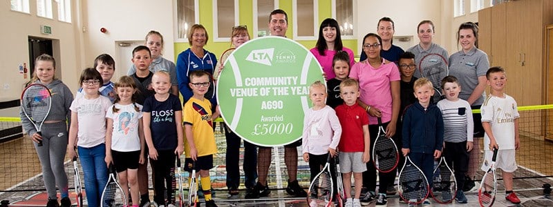 Adults and children holding tennis rackets and a community of the year award