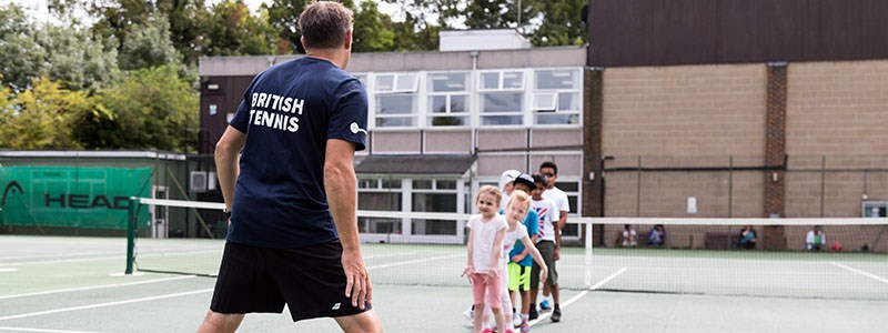 A coach coaching a group of young tennis students