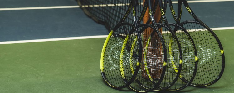 image of 5 black and yellow tennis dunlop  rackets leaning against a tennis net