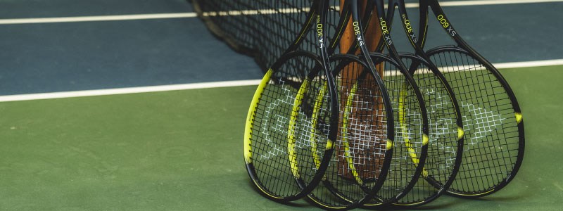 image of 5 black and yellow tennis dunlop  rackets leaning against a tennis net