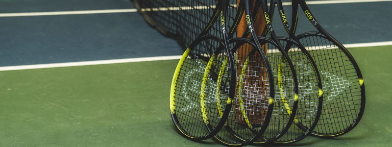 image of 5 black and yellow tennis dunlop rackets leaning against a tennis net