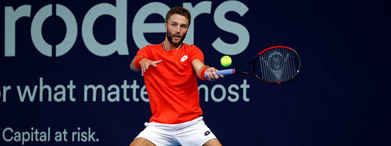 action shot of liam broady on court racket in air about to hit the ball