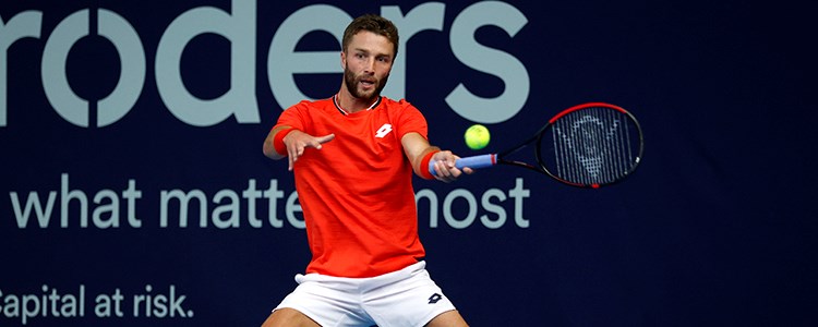 action shot of liam broady on court racket in air about to hit the ball