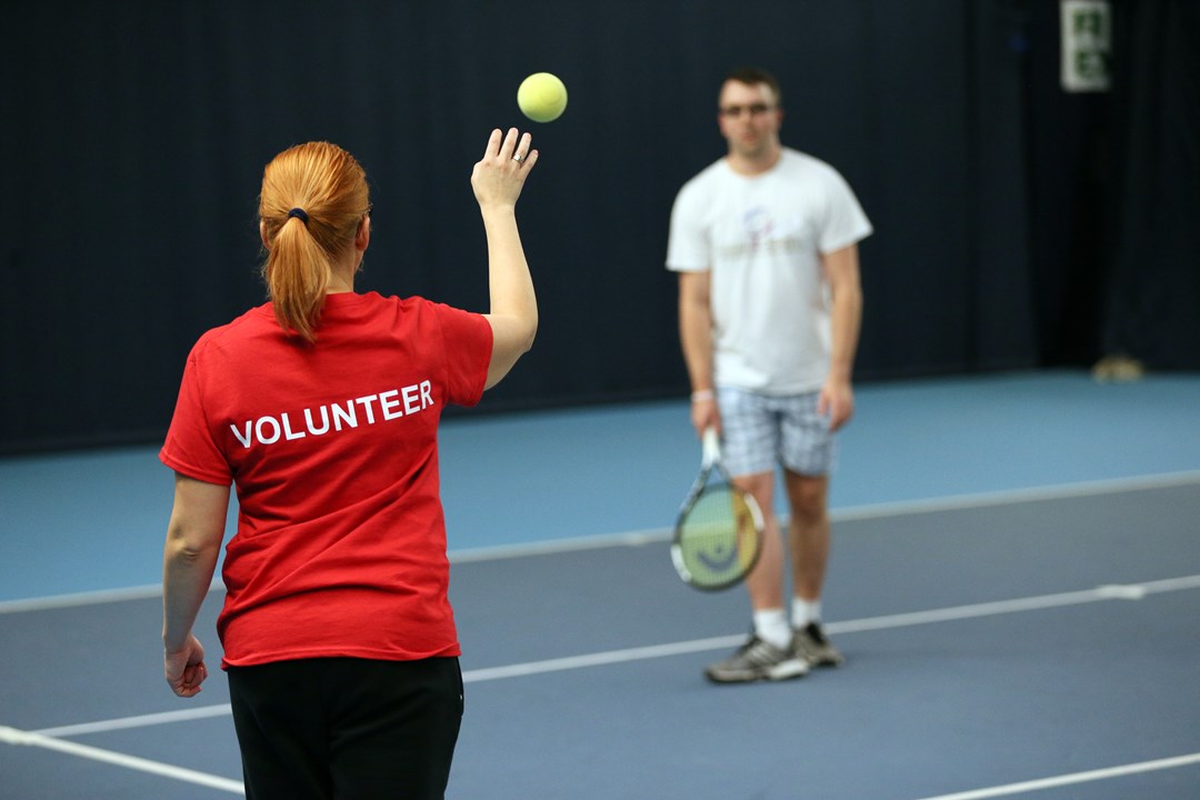 Volunteer helping visually impaired tennis players