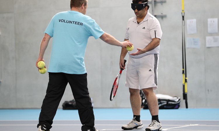 Volunteer hands a tennis ball to a visually impaired player