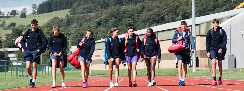 Tennis players at the GB national tennis academy at Stirling University walking on an athletic track with tennis bags on back