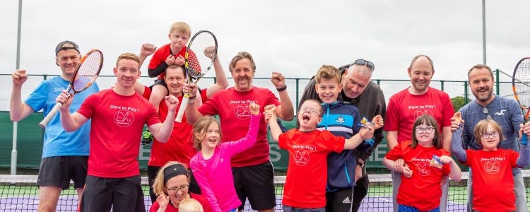 adults and kids lined up in front of a tennis net laughing and smiling for a photo