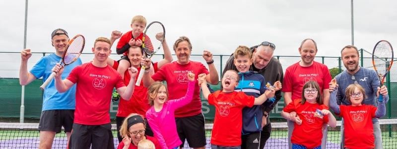 adults and kids lined up in front of a tennis net laughing and smiling for a photo