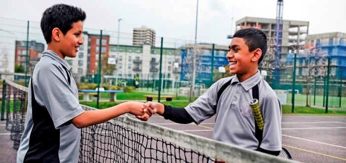 Two boys shaking hands at a tennis net