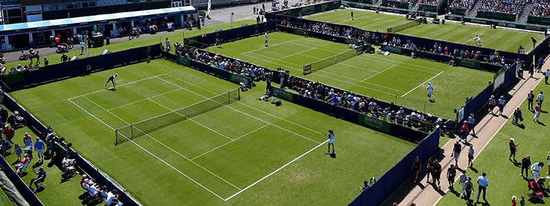 A bird's-eye view of three grass courts at Surbiton Racket & Fitness Club with matches in progress