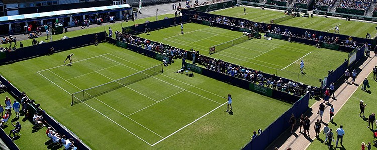 A bird's-eye view of three grass courts at Surbiton Racket & Fitness Club with matches in progress