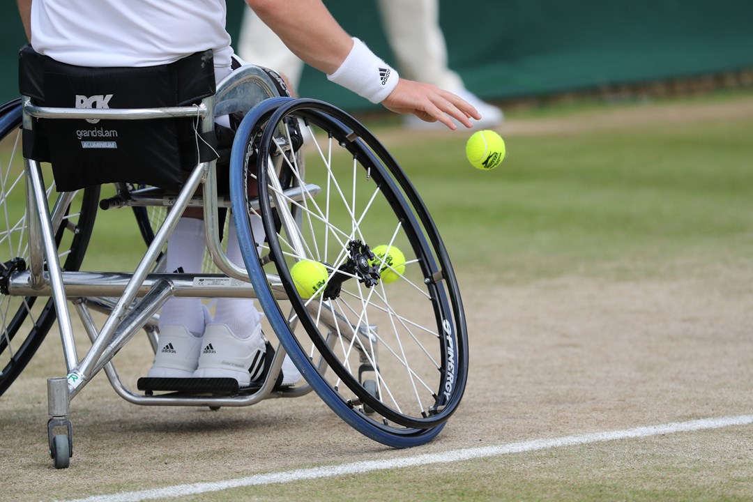 Close up of a wheelchair player bouncing the ball before serving on a grass court