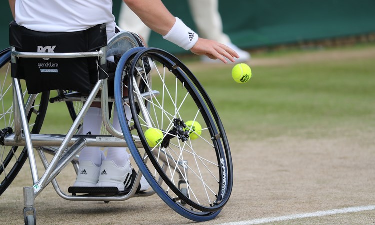 Close up of a wheelchair player bouncing the ball before serving on a grass court