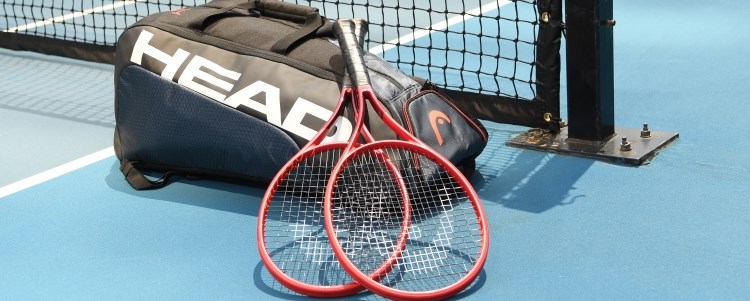 Two tennis rackets laying on top of a head branded bag on a tennis court