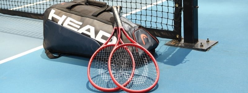 Two tennis rackets laying on top of a head branded bag on a tennis court
