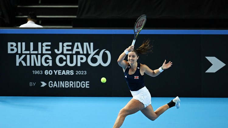 Jodie Burrage hitting a forehand on court in front of a Billie Jean King Cup advertisement board at the Copper Box Arena