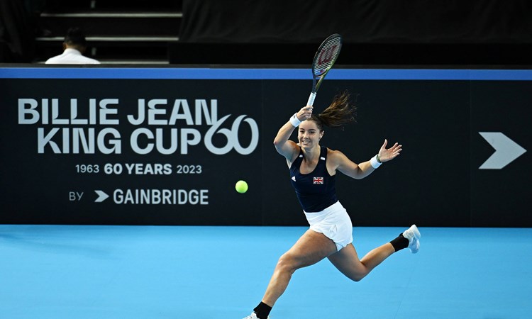 Jodie Burrage hitting a forehand on court in front of a Billie Jean King Cup advertisement board at the Copper Box Arena