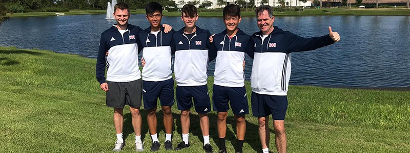 5 members of the GB team standing on grass in front of a pond with blue and white GB jackets on
