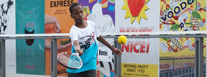 junior player wearing streetgames shirt hitting a forehand 