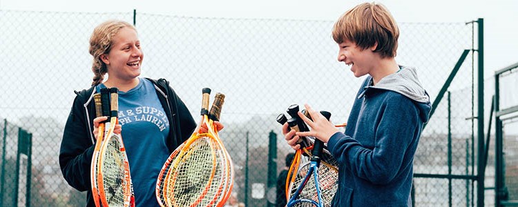 two children smiling holding tennis rackets