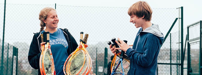 two children smiling holding tennis rackets