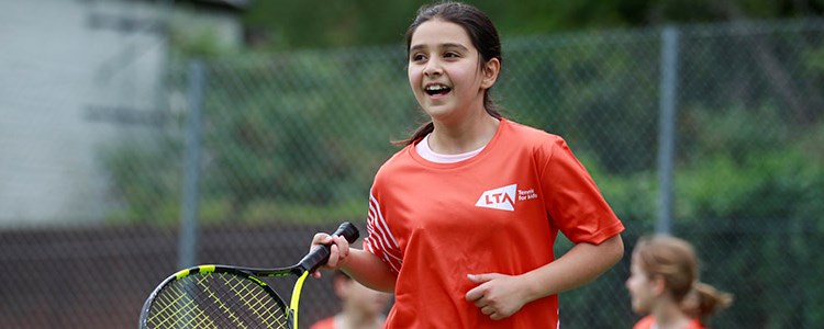 junior player on courting holding racket wearing a red LTA tennis top