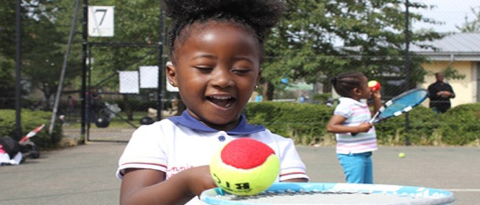 A small child with a tennis ball balancing on her racket