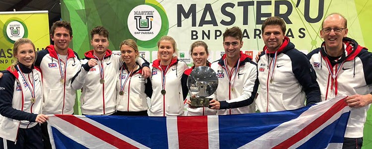 GB unviersity team standing in a line with medals and holing a trophy and holding big GB flag at the front