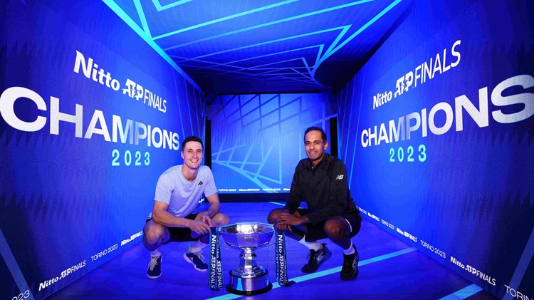 Joe Salisbury and Rajeev Ram crouching down next to the Nitto ATP Finals trophy with a digital screen saying Champions behind them