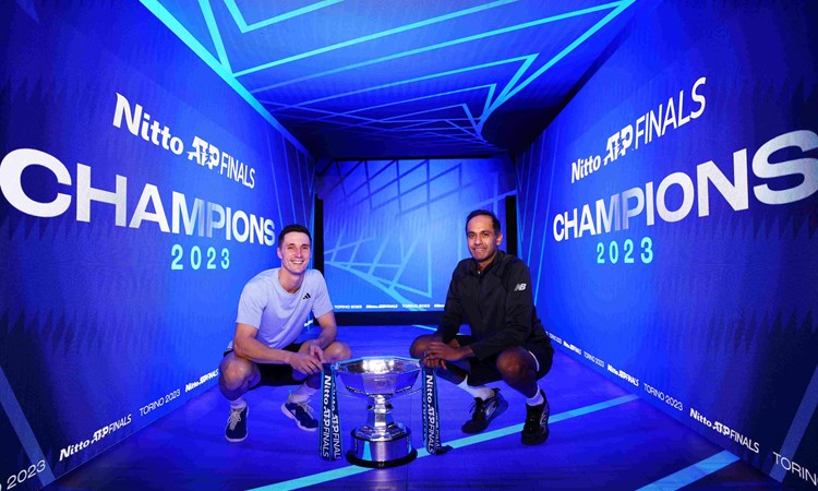 Joe Salisbury and Rajeev Ram crouching down next to the Nitto ATP Finals trophy with a digital screen saying Champions behind them