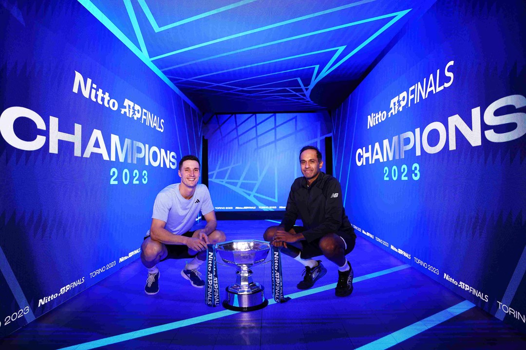 Joe Salisbury and Rajeev Ram crouching down next to the Nitto ATP Finals trophy with a digital screen saying Champions behind them