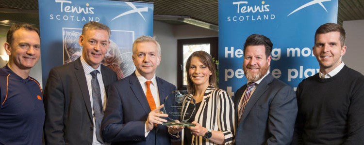 a group of winners lined up with two holding a glass tennis scotland trophy