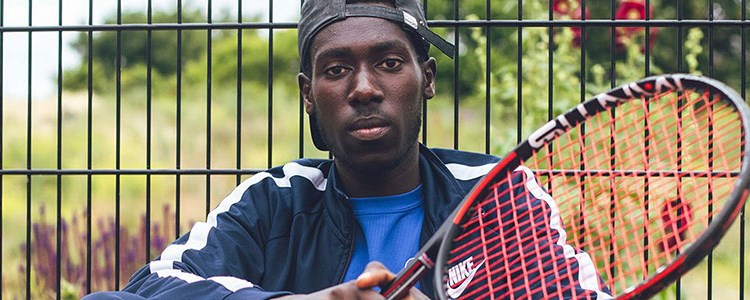 close up of Arum Akom sitting in front of a fence with tennis racket in hand