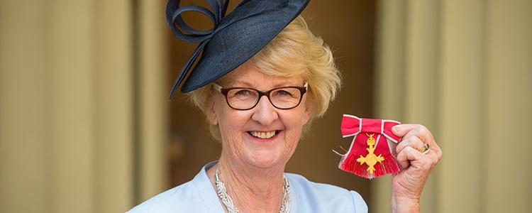 Cathie Sabin honoured with an OBE in 2016, holding it up to the camera